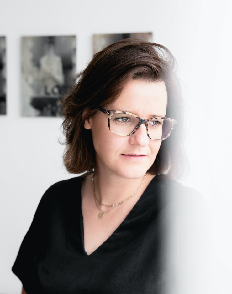 Mag. Anna Lindner, LL.M. mit Brille im Portrait und Gemälde im Hintergrund